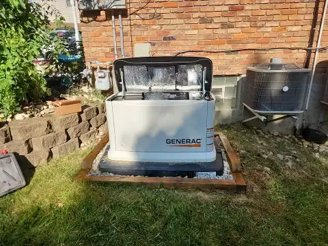 A Generac standby generator installed outside a brick house, positioned on a concrete pad with its lid open, near an air conditioning unit.