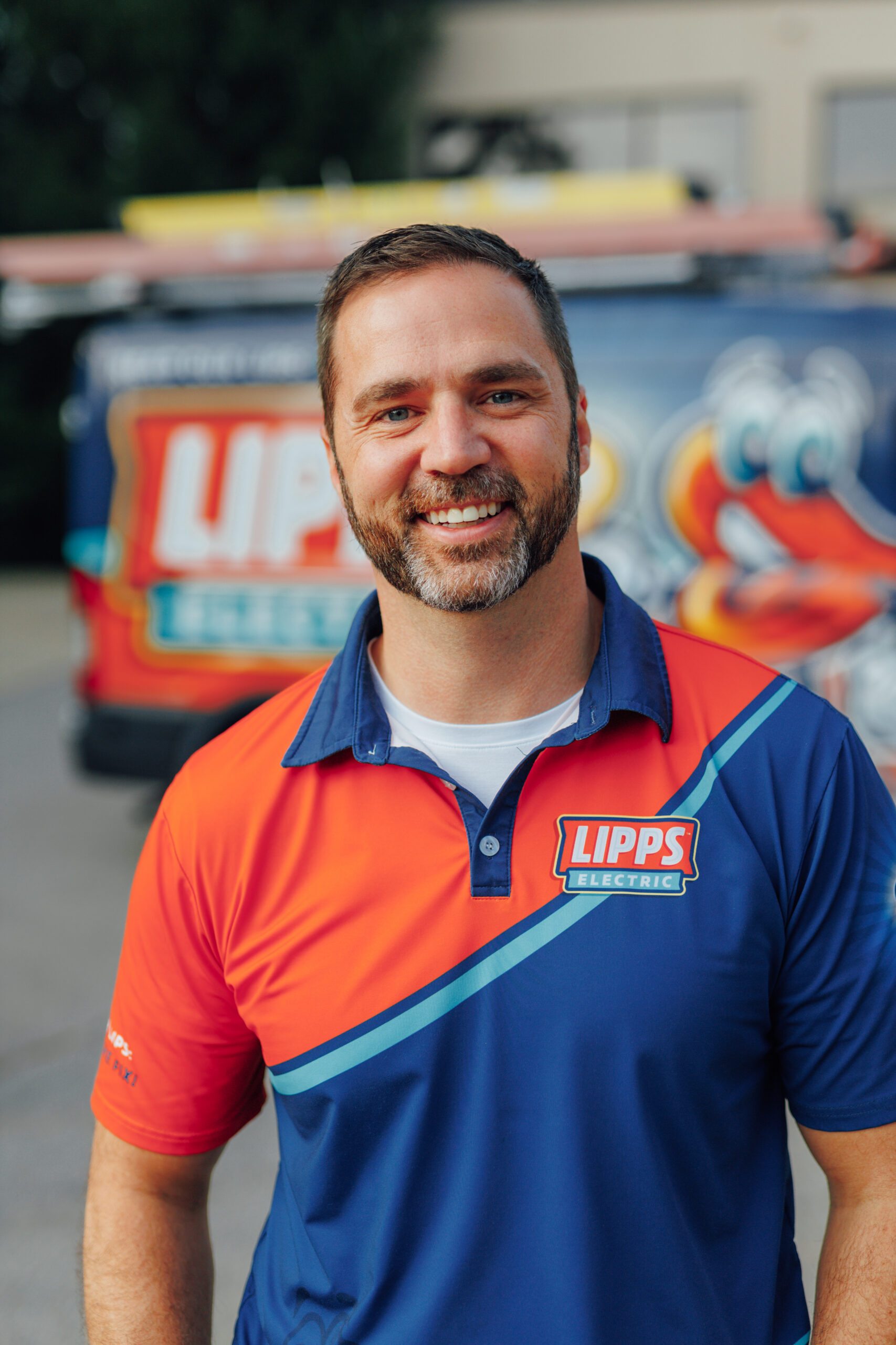 Man wearing a Lipps Electric uniform stands smiling in front of a branded service van outdoors.