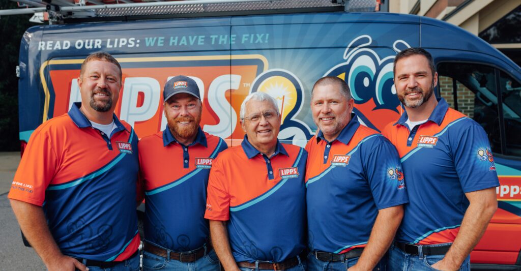 Five men in matching blue and orange uniforms stand in front of a branded service van, smiling at the camera.